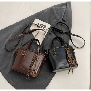Detail of vintage bucket bags with gold rivets and woven pendants on grey blazer