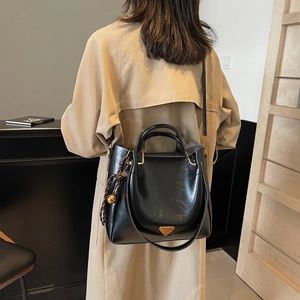 Chic black glossy leather tote bag with metallic triangle logo and decorative scarf charm