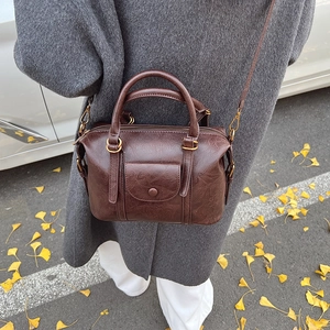 Vintage dark brown Boston bag with golden hardware and shoulder strap in autumn setting