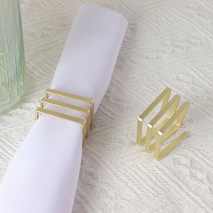 Modern matte gold square napkin rings set shown with a white cloth on a textured surface