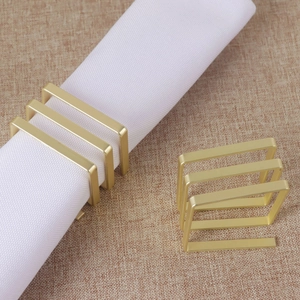 Modern square matte gold napkin rings set with sleek metallic hollow design on linen