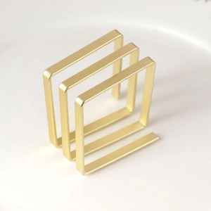 Close-up of matte gold square napkin ring with tiered metallic frame structure