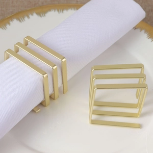 Close-up of matte gold square napkin ring on white fabric napkin in a ceramic plate