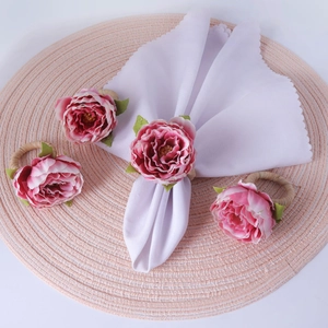 Pink faux rose napkin rings with straw base and white cloth on a woven placemat