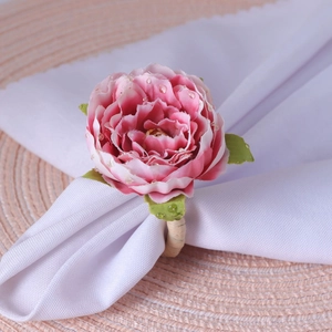 Pink artificial rose napkin ring with realistic water drops and woven base on white fabric