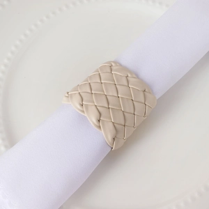 Gros plan d'un rond de serviette en similicuir tressé crème sur une assiette blanche