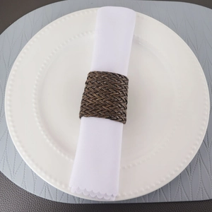 Détail d'un rond de serviette en cuir PU marron tressé sur un tissu blanc et assiette