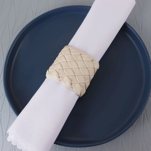 Rond de serviette artisanal en cuir PU tressé beige sur une serviette blanche et plat