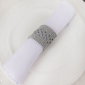Détail d'un rond de serviette tressé gris sur une serviette blanche et plat céramique
