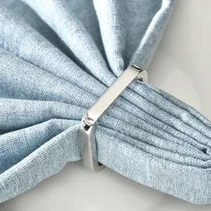 Modern silver polished square metal napkin ring with elegant light blue fabric on white desk