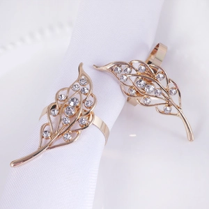 Detail of leaf-shaped gold napkin rings with hollow rhinestones on white cloth