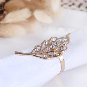 Close-up of golden hollow leaf napkin ring with sparkling rhinestones on white cloth