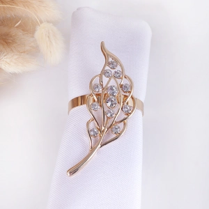 Close-up of golden leaf napkin ring with clear rhinestones on a white fabric napkin