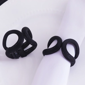 Close-up of black mesh metal napkin rings in minimalist knot design on white dinnerware