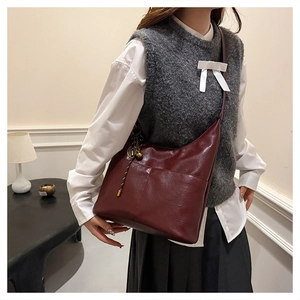 Detail of burgundy half-moon crossbody bag with stitching and metallic pendant charm
