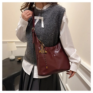 Detail of burgundy leather tote bag with a unique tennis racket metal pendant and adjustable strap