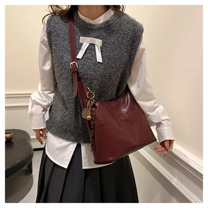 Detail of burgundy half-moon tote bag with gold tennis racket charm and adjustable strap
