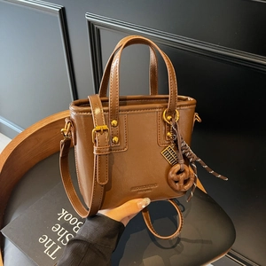 Brown vintage bucket tote bag with top handles and adjustable strap on a wooden chair