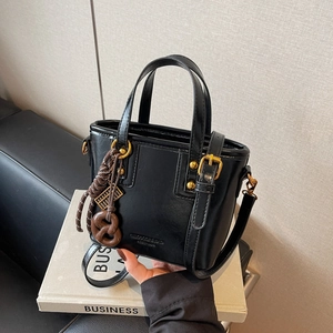 Vintage black leather bucket bag with gold accents and decorative charms on a prop book