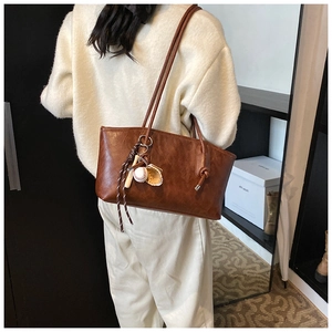 Brown leather tote bag detail with unique baseball themed charms and long shoulder straps
