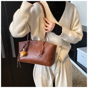 Brown leather tote bag featuring a decorative strawberry pendant and knot handle detail