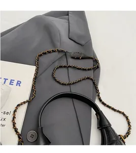 Détail du sac en cuir matelassé noir avec chaîne dorée sur fond de costume gris