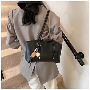 Detail of minimalist black tote bag with baseball charm on a casual grey suit