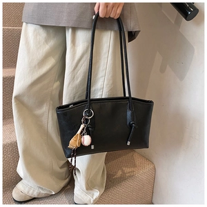 Close-up of black leather tote bag with unique baseball glove pendant on a model