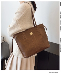 Detail of a large brown leather tote bag with a gold square buckle and drawstring