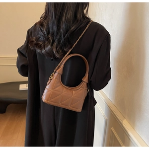 Détail d'un sac matelassé marron avec chaîne dorée porté sur un manteau d'hiver noir