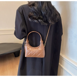 Sac bandoulière matelassé marron avec chaîne dorée porté par un mannequin en costume noir