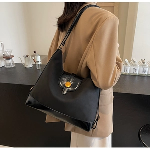 Vue latérale d'un grand sac cabas noir avec fermoir doré porté par un mannequin