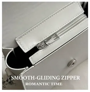 Detail view of smooth silver metal zipper and magnetic buckle on white leather bag