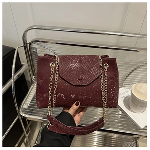 Detail of burgundy snakeskin texture handbag with golden chain strap and magnetic flap