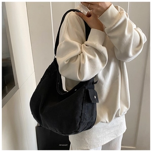Detail of black crescent canvas bag showing functional side pocket and metal button