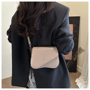 Detail van beige zadeltas met asymmetrische flap en modieus logo op een model