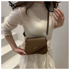 Detail of brown matte leather saddle bag with asymmetric flap and metal lettering logo