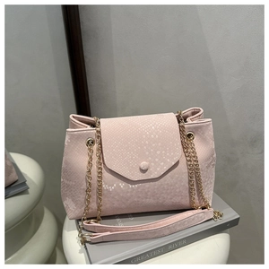 Détail du sac en cuir rose à motif serpent avec chaîne dorée sur des livres déco