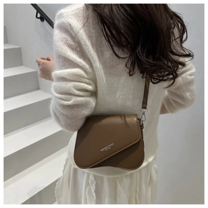 Bruine zadeltas met asymmetrische flap en logo getoond door model op witte trap