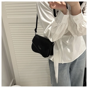 Detail of minimalist black leather crossbody bag with white lettering shown on model