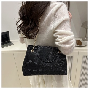 Détail d'un sac à bandoulière noir motif serpent avec chaîne dorée sur un pull en maille