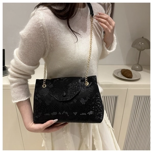 Detail view of black snakeskin embossed shoulder bag with gold chain strap worn by model
