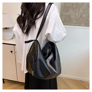 Model wearing large black tote bag with side zipper and glossy finish in minimalist room