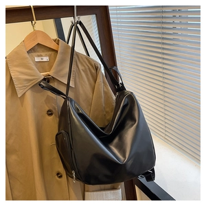 Detail of a large black tote bag with side zipper pocket hanging on a khaki trench coat