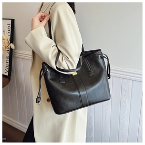 Detail of black leather tote bag featuring side drawstrings and gold metal hardware