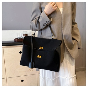 Detail view of black suede tote bag with golden metal locks and leather tassel charm