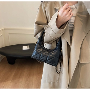 Gros plan sur un sac en cuir noir matelassé avec chaîne dorée porté par un mannequin