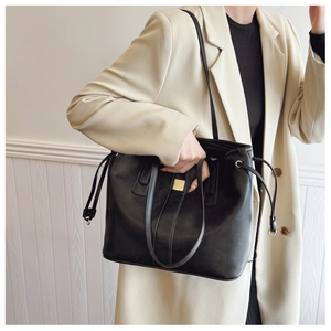 Detail of black faux leather tote bag with gold metal buckle and side drawstring design