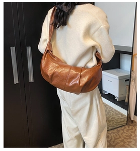 Detail of caramel brown pleated crescent bag showing glossy faux leather and slouchy shape