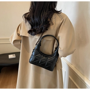 Sac croissant noir matelassé avec chaîne dorée porté sur un trench-coat classique